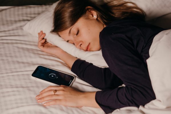 Girl asleep in bed with mobile phone next to her.